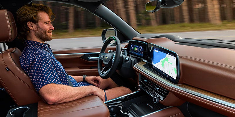 Man sitting in a 2025 Chevrolet Suburban driver's seat. He is looking at the GPS screen and appears comfortable and relaxed.