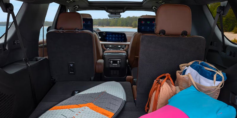 Interior view of the 2025 Chevrolet Suburban loaded with beach bags, towels and a surfboard. Two of the passenger seats are lowered for the board.
