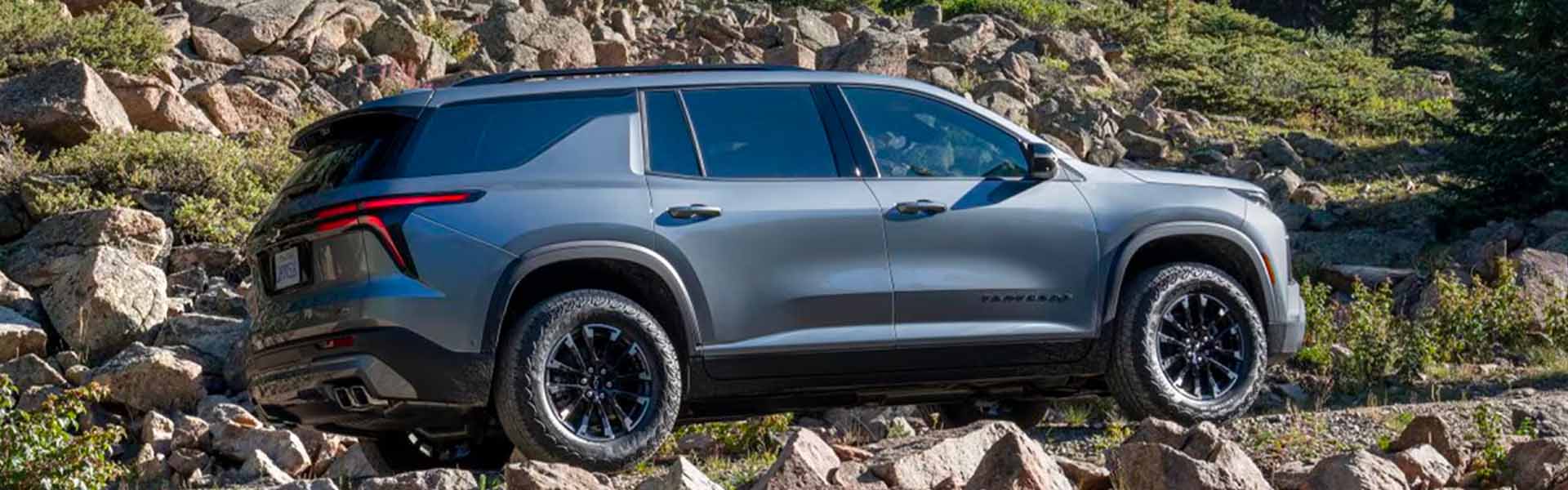 Side view of 2025 Chevrolet Traverse driving over large rocks on a grassy hill